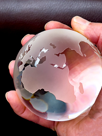 A caucasian hand is holding a glass ball with the African and Europian continents prominently displayed.