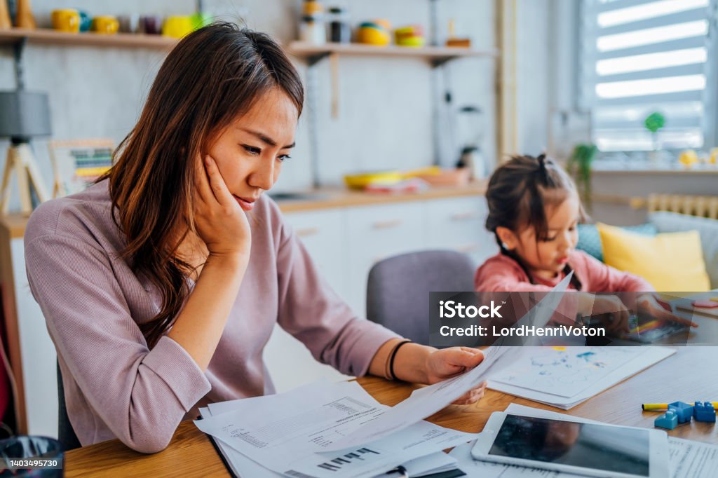 Stressed mother going through her finances Young stressed mother checking her finances while her daughter is playing next to her Finance Stock Photo