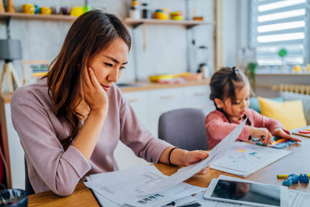 Stressed mother going through her finances Young stressed mother checking her finances while her daughter is playing next to her struggle stock pictures, royalty-free photos & images