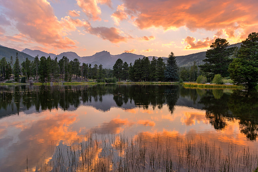 A panoramic Summer sunset view at Sprague Lake, with high peaks of Continental Divide rising at shore, Rocky Mountain National Park, Colorado, USA.