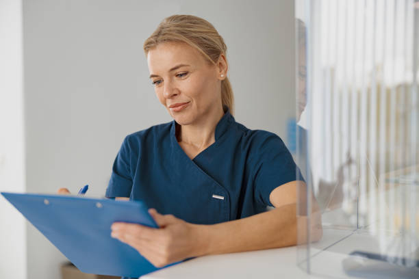 istock Smiling doctor making notes on clipboard standing near reception in clinic hall 1403502325