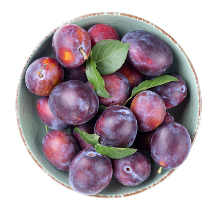 Ripe plums and leaves in a bowl isolated on white background. Harvesting. Top view. File contains clipping path.
