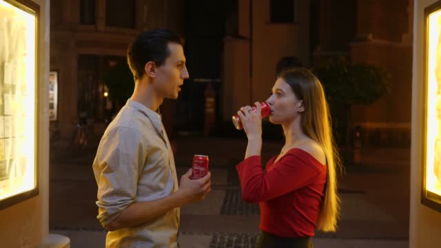 Young people couple stay talking drinking red cola cans during night city date walk