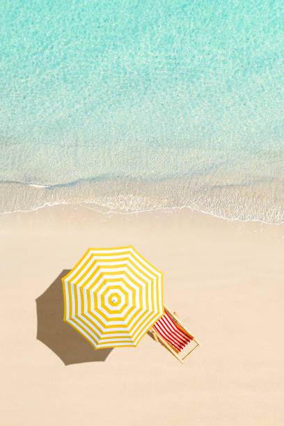 Top view of sunbed, lounge, yellow umbrella, SUP board for surfing on the shore on tropical Seychelles sand beach. Blue, turquoise transparent water surface of ocean, sea, lagoon. Aerial, drone view. vertical stock photo