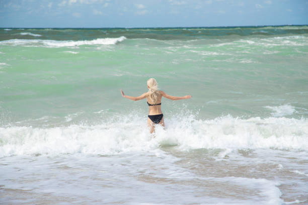single happy young woman in swimsuit walking at sea surf with splashes