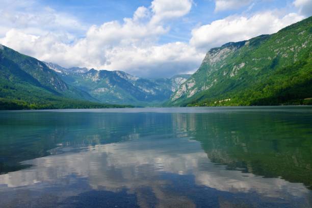 blick auf den bohinjer see, umgeben von bergen in den julischen alpen und im nationalpark triglav, slowenien im sommer und ein spiegelbild der berge und der wolken im wasser - julian alps mountain lake reflection stock-fotos und bilder