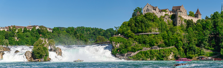 Schaffhausen, Switzerland - 12.06.2022: People admiring the Rhine Falls from the boat that brings tourist to the exclusive terrace in the middle of the waterfall. The falls are located on the High Rhine, near the town of Schaffhausen, and are the largest plain waterfall in Europe.