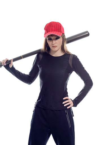 Aggressive Caucasian Female Baseball Player Athlete Holding Bat Behind Shoulders Wearing Sport Outfit And Red Cap Against Pure White background. Vertical Image