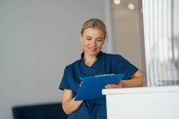istock Smiling doctor making notes in clipboard standing near reception in clinic hall 1403508635