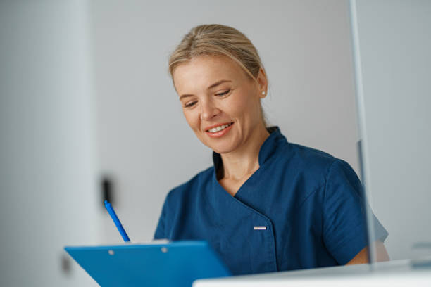 istock Smiling doctor making notes in clipboard standing near reception in clinic hall 1403508637