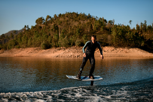 man in black wetsuit riding on river water on a foil wakeboard on beautiful landscape background.