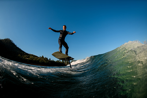 athletic man in a black skillfully balances on the wave on a foil wakeboard. Water sports activity.
