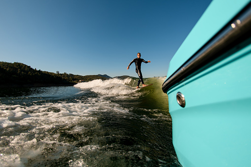 great view from a boat on active man in black wetsuit on a wakesurf riding on a splashing wave