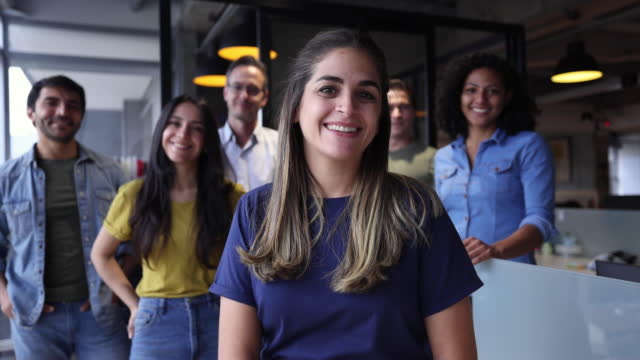 Happy group of Latin American workers standing behind female manager all facing camera smiling at the office