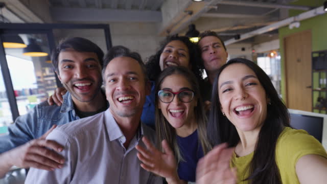 Diverse coworkers having fun at the office goofing around during a video call facing camera talking and smiling