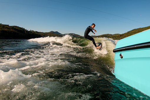 great view from a boat on active man in black wetsuit on a wakesurf skillfully riding on a splashing wave