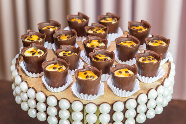 Chocolate cups with mousse and passion fruit seeds for party on wooden stand with pearl details