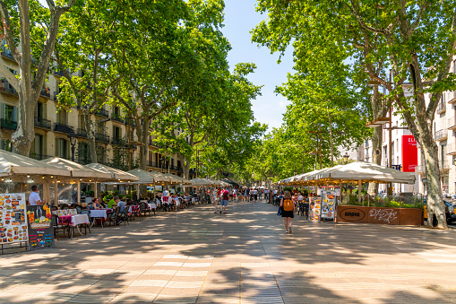 Tourists enjoying the tree lined La Rambla, a busy street in the historic district withs shops and sidewalk cafes.