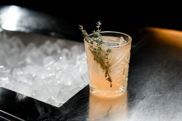 selective focus on rosemary branch which garnished glass of cold cocktail - transparent holding glass focus on foreground imagens e fotografias de stock