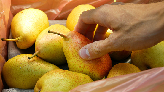 Many beautiful pears in a trading box and a buyer's hand takes one
