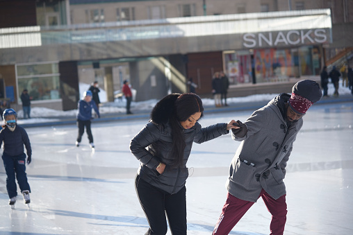 Toronto Ontario, Canada- February 8th, 2022: A girlfriend and boyfriend holding hands while ice skating at Toronto City Hall's Nathan Phillips Square.