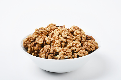 Peeled walnuts in a white bowl on the white background
