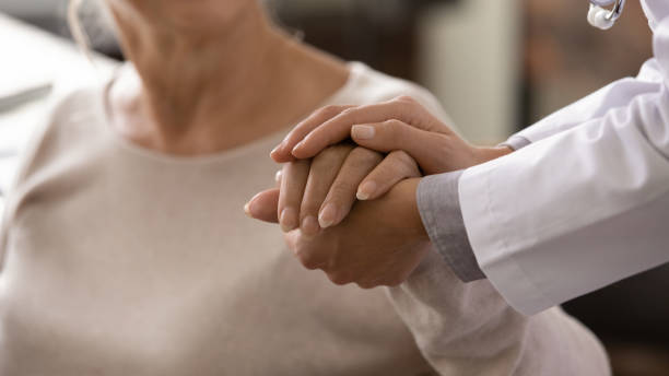 Female doctor in white coat holding hand of senior patient stock photo