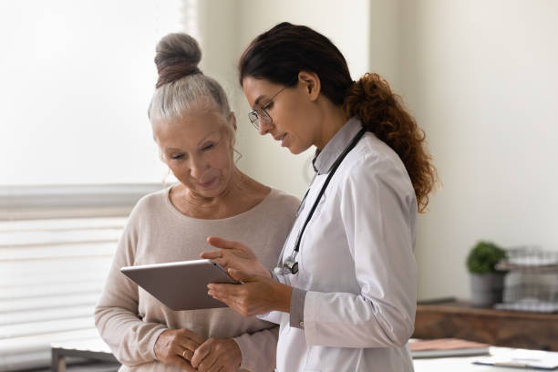 Serious GP doctor showing tablet screen to old female patient stock photo