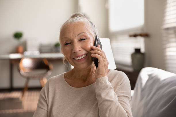 dame âgée heureuse parlant au téléphone portable, passant un appel de la maison - grandmother women one person senior adult photos et images de collection