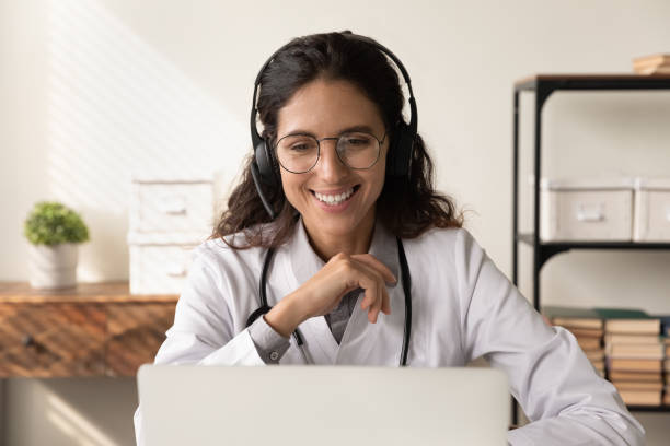 счастливая дружелюбная женщина-врач в наушниках общается с пациентом - laptop doctor using computer nurse стоковые фото и изображения