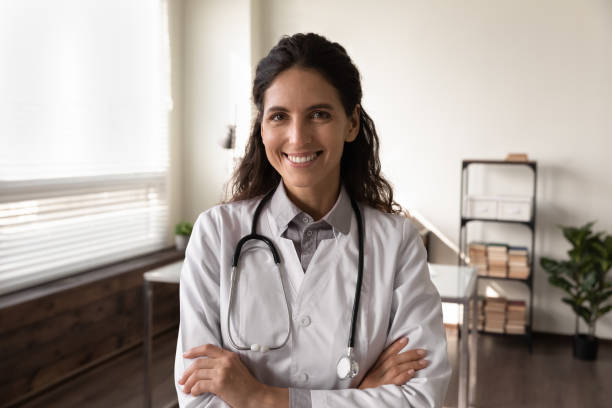 Happy female GP doctor in white coat looking at camera stock photo