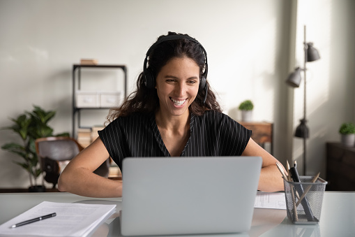 Feliz mujer de negocios millennial con auriculares, trabajando en una computadora portátil photo