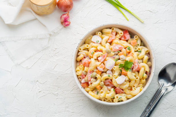 Homemade macaroni salad with elbow pasta Homemade macaroni salad with elbow pasta, onion, carrot, tomato, green peas and mayonnaise dressing in a white bowl on a white wooden table.Top view macaroni stock pictures, royalty-free photos & images