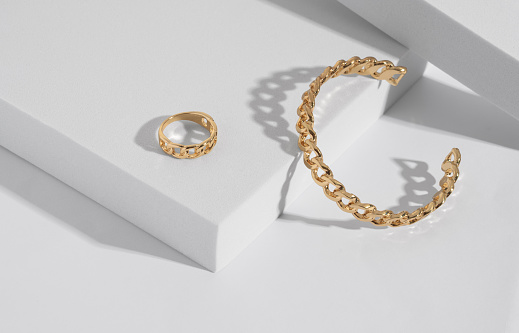 Chain shape golden modern bracelet and ring on white podium with copy space