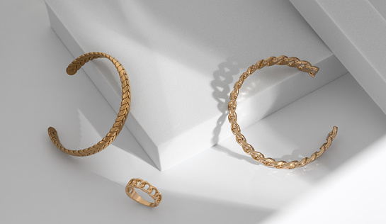 Shiny Modern gold braid shape and chain shape bracelets and ring on white geometric background with copy space