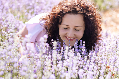 Romantic close-up portrait of curly girl enjoying scent of lavender, closed her eyes in field on sunny day. Girl walks pink field of flowers. Digital detox, pleasure ofslow life. Soft Selective focus