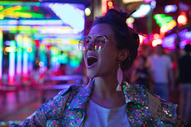 네온 조명으로 도시 거리에서 빛나는 스팽글이있는 재킷을 입은 세련된 여성 - city defocused lighting equipment illuminated 뉴스 사진 이미지