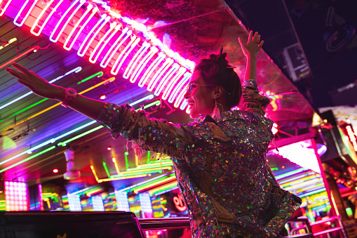 Young stylish woman wearing jacket with shining sequins on the city street with neon lights