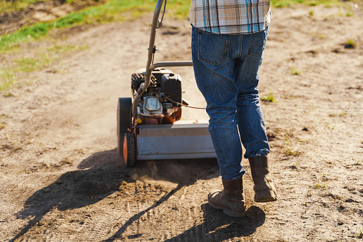 Closeup shoot of man using aerator machine to scarification and aeration of lawn or meadow