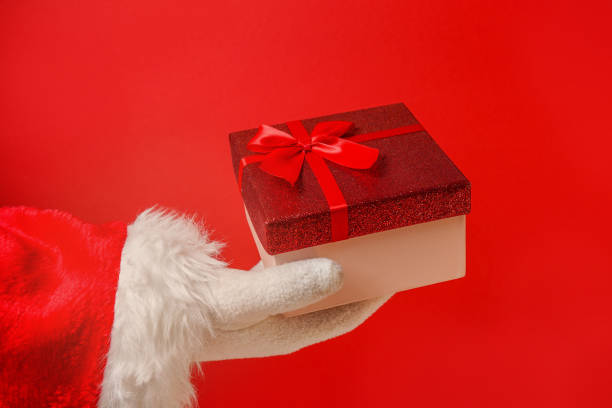 istock Santa Claus hand holding gift box on red background 1403528815