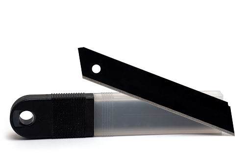Close up of plastic package and dark sharp metal razor blade placed in front of it for use in knives with interchangeable snap off blades on white background