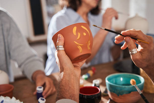 Senior man holding clay pot and brush while drawing patterns on it at the loft studio stock photo
