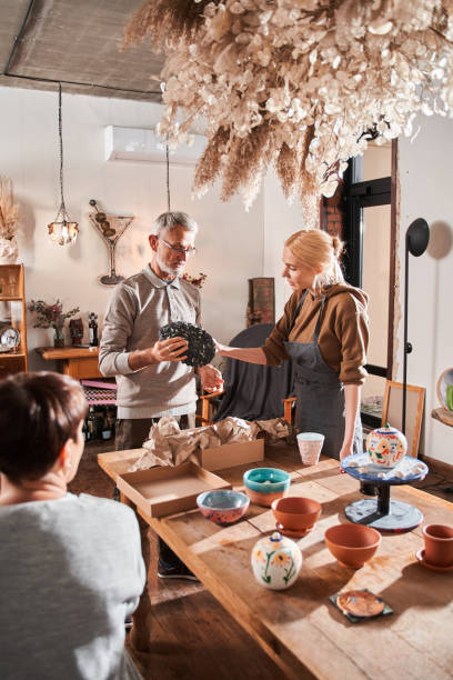 istock Female teacher wearing apron standing at the master class and explaining to elderly man 1403529769