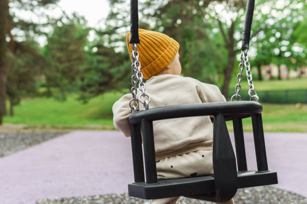 istock Cute baby boy sitting on a swing in public park 1403529949