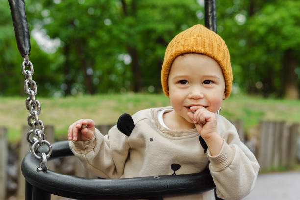 Cute baby boy sitting on a swing in public park stock photo