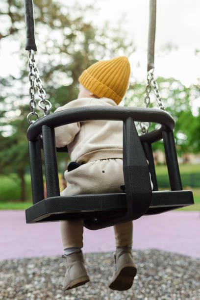 istock Cute baby boy sitting on a swing in public park 1403529979