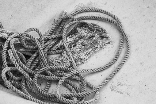 Black and white closeup shot of shabby coil of nautical rope tangled on the bottom of a fishing boat hull.