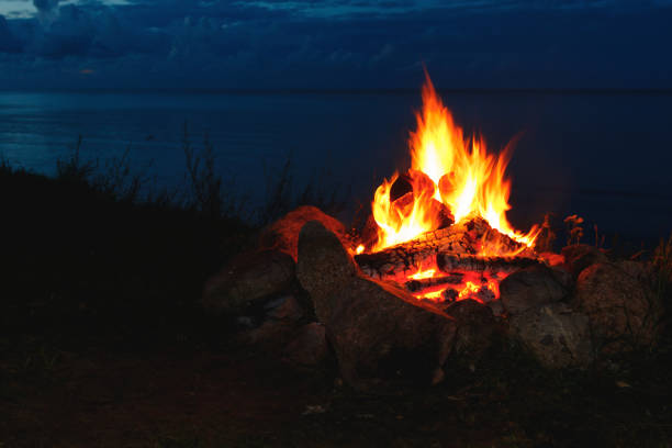 Closeup shot of a campfire brightly burning at night in an outdoors camp with a calm sea on background.