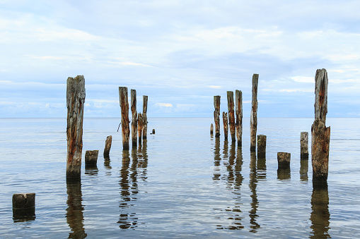 A beautiful shot of a a calm sea scenery with broken pier poles sticking out of water on horizon background.