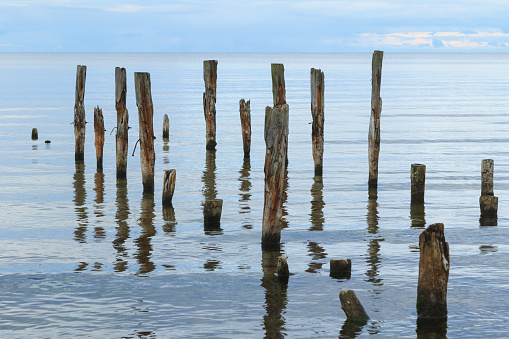 A beautiful shot of a a calm sea scenery with broken pier poles sticking out of water on horizon background.